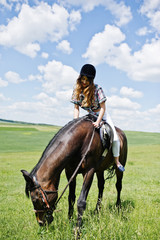 Young pretty girl riding a horse on a field at sunny day.