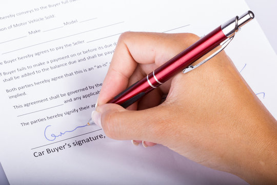 Car buyer signature - contract closeup, hand holding a pen above the legal document