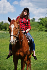Young pretty girl riding a horse on a field at sunny day.