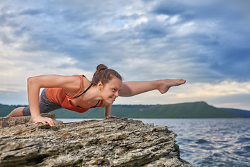Healthy woman practicing yoga on the rock against beautiful landscape with river.