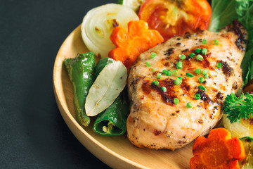 Homemade chicken breast barbecue on wood plate served with grilled vegetables. Delicious chicken barbecue and grilled vegetables for lunch or dinner. Roast chicken breast on granite table.