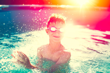 Obraz na płótnie Canvas Little kid in goggles splashing in swimming pool, summer sunset, vintage