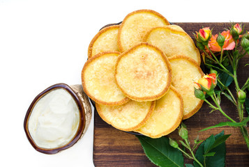 Breakfast of the day off - golden pancakes with sour cream. A wooden board, a rose flower. White background, top view. Homemade food