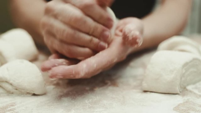 Close-up of woman baker rolling raw dough for buns preparation. 