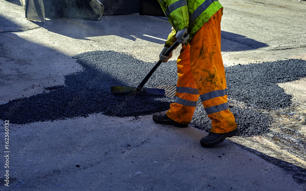 Wall mural worker leveling fresh asphalt during asphalt pavement repair or construction works