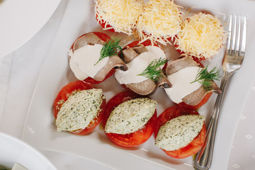 Тарелка с закуской из грибов, помидор, мяса и сыров на сервированном и накрытом столе в ресторане