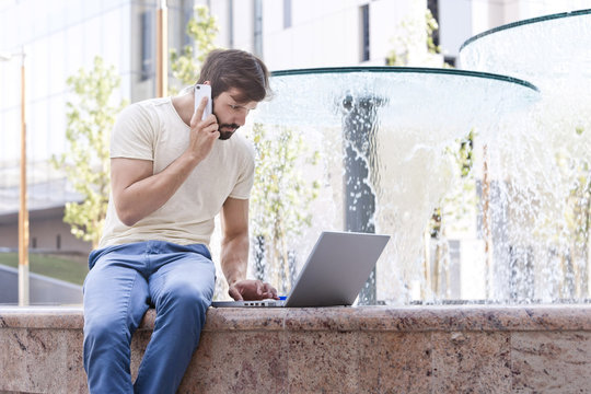 Male university student using mobile phone and laptop