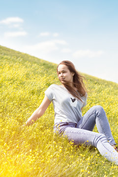 Young girl teenager on a lawn field with yellow flowers. Long chestnut hair. Sunshine, springtime, blue sky. Coloring and processing photos with soft selective focus. Shallow depth of field.