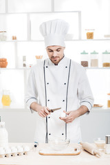 Chef in uniform breakseggs in bowl to prepare dough in kitchen