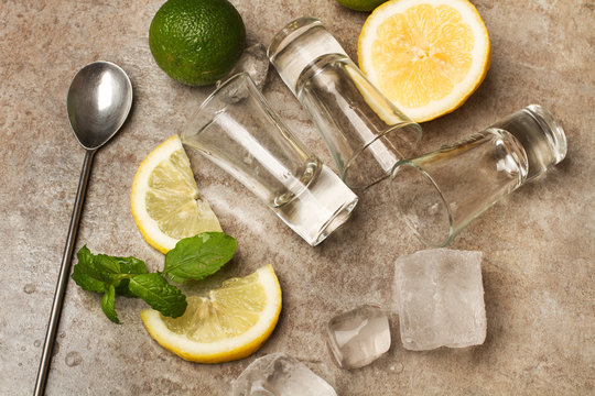 Lim&oacute;n, lima, bebida, vaso, cuchara y hielo sobre una mesa gris. Vista superior