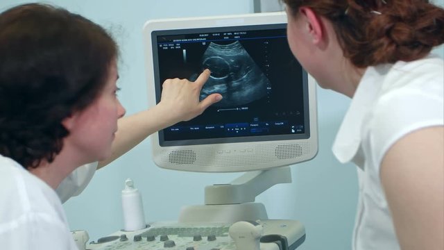 Gynecologist and pregnant patient looking at ultrasonogram showing fetus