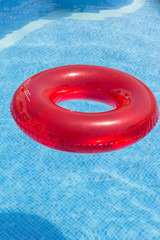 Flotador rojo de playa sobre piscina con fondo azul claro.