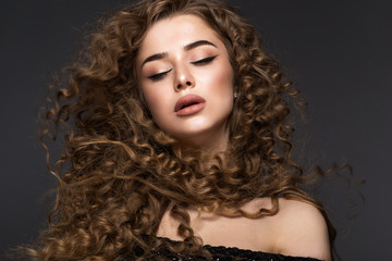 Beautiful brunette girl in move with a perfectly curly hair, and classic make-up. Beauty face. Picture taken in the studio on grey background.