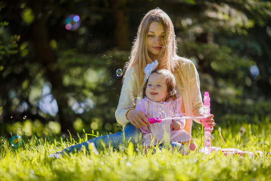 A young mother with her daughter blowing soap bubbles in the park
