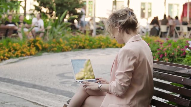 Attractive blonde white woman working freelance with laptop and smartphone in park at sunny day