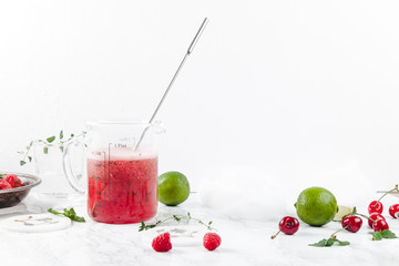 Pitcher with refreshing watermelon and strawberry lemonade with lime juice, ginger and honey on marble table and white background. Summertime beverage concept. Copy space