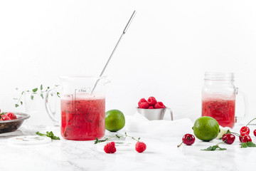 Pitcher with refreshing watermelon and strawberry lemonade with lime juice, ginger and honey on marble table and white background. Summertime beverage concept. Copy space