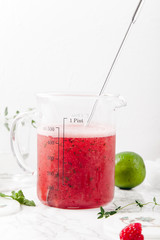 Pitcher with refreshing watermelon and strawberry lemonade with lime juice, ginger and honey on marble table and white background. Summertime beverage concept. Copy space