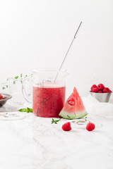 Pitcher with refreshing watermelon and strawberry lemonade with lime juice, ginger and honey on marble table and white background. Summertime beverage concept. Copy space