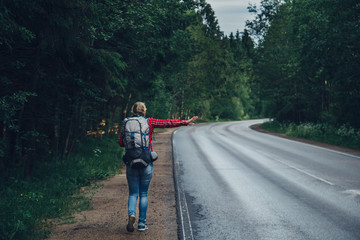 Obraz premium Lonely girl hitchhiking on the road with a backpack.