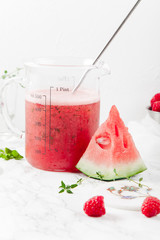 Pitcher with refreshing watermelon and strawberry lemonade with lime juice, ginger and honey on marble table and white background. Summertime beverage concept. Copy space