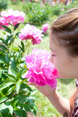 Fototapeta premium Girl enjoying of pink Minuet peony smell in formal garden