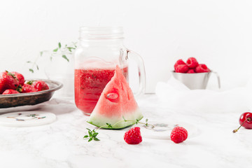 Glass jar cup with refreshing watermelon and strawberry lemonade with lime juice, ginger and honey on marble table and white background. Summertime beverage concept. Copy space