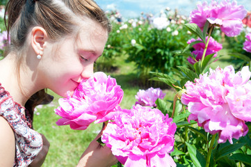 Obraz na płótnie Canvas Pretty teenage girl smelling pink blossoming peony flowers in park