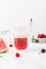 Glass jar cup with refreshing watermelon and strawberry lemonade with lime juice, ginger and honey on marble table and white background. Summertime beverage concept. Copy space