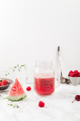 Glass jar cup with refreshing watermelon and strawberry lemonade with lime juice, ginger and honey on marble table and white background. Summertime beverage concept. Copy space