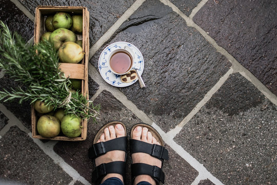 Feet in sandals standing near fruit basket