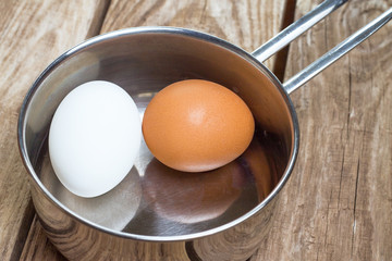 Two eggs in saucepan on wooden table
