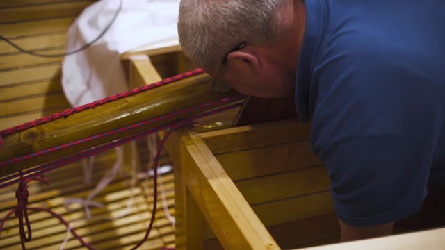 Mature master in glasses with assistant working with newly homemade wooden boat or sailboat in workshop