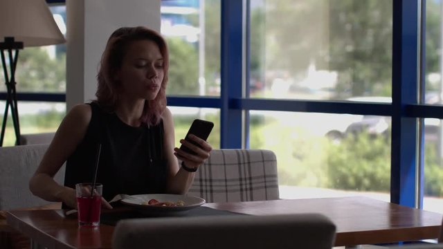 Business woman eats at a cafe and uses a smartphone.