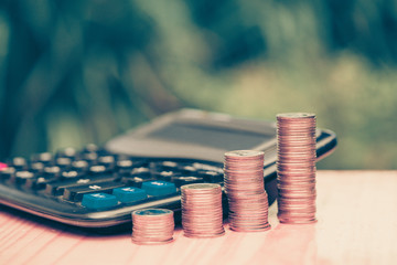 Growing coins and calculator on wood with green tree bokeh background. vintage tone