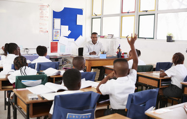 Child raising hand to teacher in an elementary school class