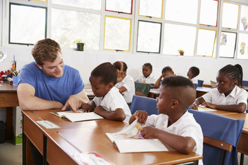 Volunteer teacher helping young girl at her desk in class