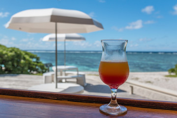 Cocktail glass in front tables with umbrella and a coral lagoon