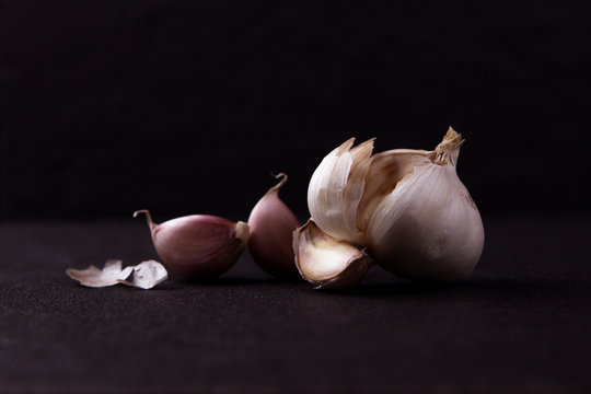  a still life arrangement of Three whole garlic bulbs grouped on black stone plate