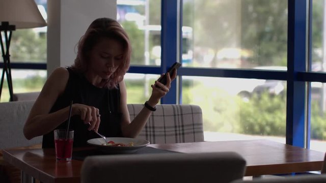 Business woman eats at a cafe and uses a smartphone.