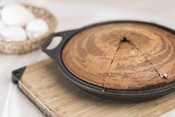 Home freshly baked zebra pie in a black pan lies on a light wooden cutting board in the background of a wicker basket with eggs in the defocus