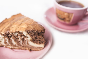 A slice of a homemade Zebra pie on a saucer mauve pink colour and a cup of tea on a saucer in a defocus on a white lace background