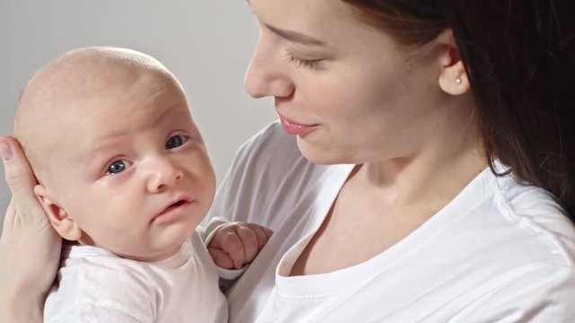Tilt up of young mother holding yawning baby boy on arms and telling something