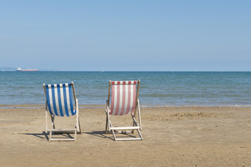 Two empty linen beach chairs one blue and one red in a sea landscape on the beach of Weymouth of the United Kingdom, facing the sea on a sunny day
