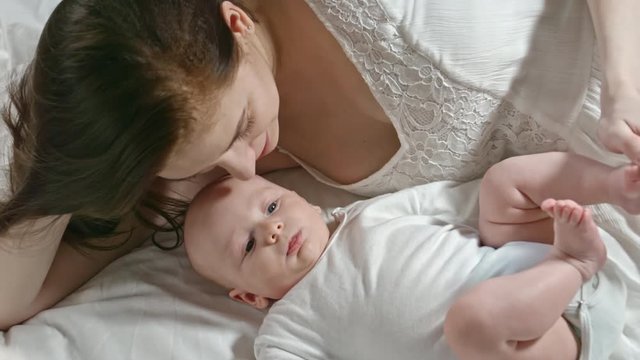 Zoom in of mother and baby lying on bed. Woman caressing little infant and telling something to him
