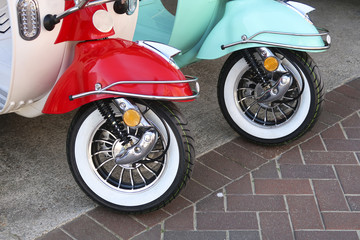 One red and one blue scooter front wheels standing parked on the street