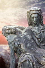 Bronze statue of Virgin Mary holding the body of Jesus Christ with sunset landscape in background