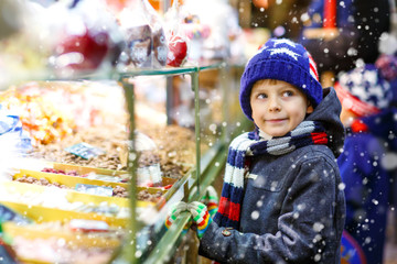 Little kid boy with gingerbread and sweets stand on Christmas market