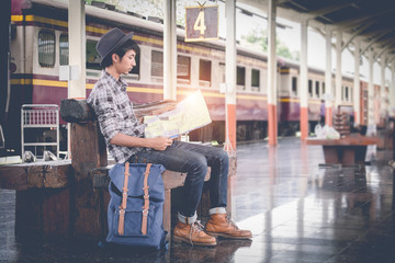Young travel sitting with map. travel bag at the train station.vintage filter effected .
