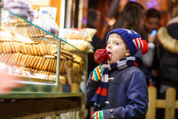 Little kid boy eating sugar apple sweets stand on Christmas market
